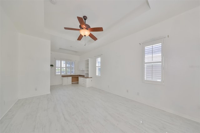 spare room featuring a raised ceiling, ceiling fan, a healthy amount of sunlight, and light wood-type flooring