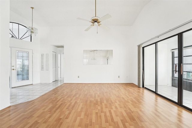 unfurnished living room featuring ceiling fan with notable chandelier, light wood-type flooring, and high vaulted ceiling