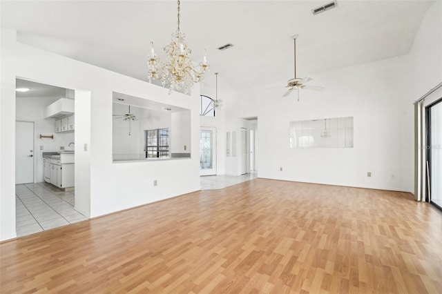 unfurnished living room featuring ceiling fan with notable chandelier, a towering ceiling, and light hardwood / wood-style flooring