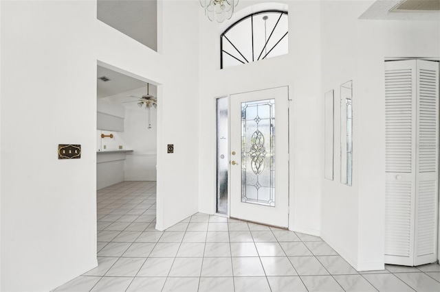 tiled foyer featuring a high ceiling and ceiling fan with notable chandelier