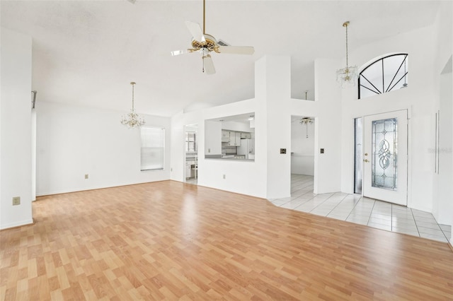 entryway with ceiling fan with notable chandelier, light wood-type flooring, and high vaulted ceiling