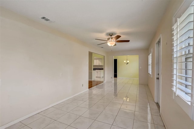 tiled spare room featuring ceiling fan with notable chandelier