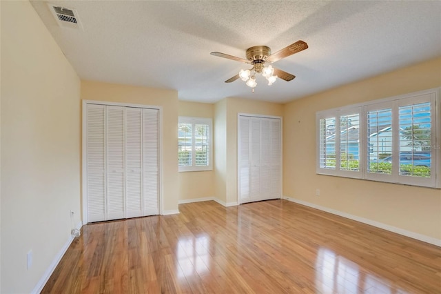 unfurnished bedroom with ceiling fan, multiple windows, multiple closets, and light hardwood / wood-style flooring