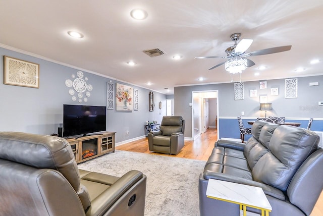 living room featuring crown molding, light hardwood / wood-style floors, ceiling fan, and a fireplace