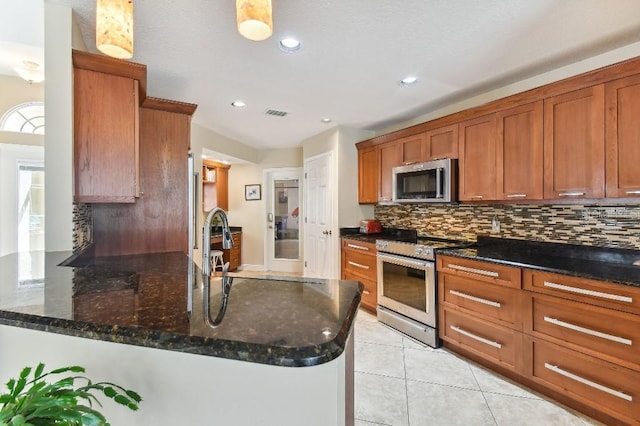 kitchen with light tile floors, tasteful backsplash, appliances with stainless steel finishes, hanging light fixtures, and dark stone countertops