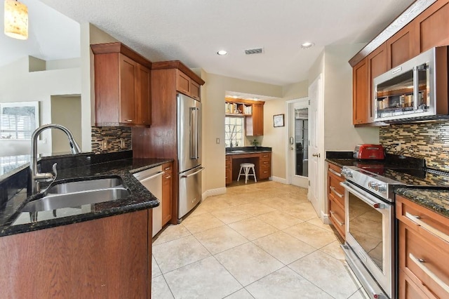 kitchen with sink, light tile floors, appliances with stainless steel finishes, dark stone countertops, and tasteful backsplash