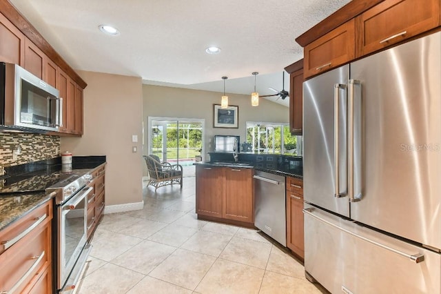 kitchen featuring light tile floors, hanging light fixtures, dark stone countertops, premium appliances, and tasteful backsplash