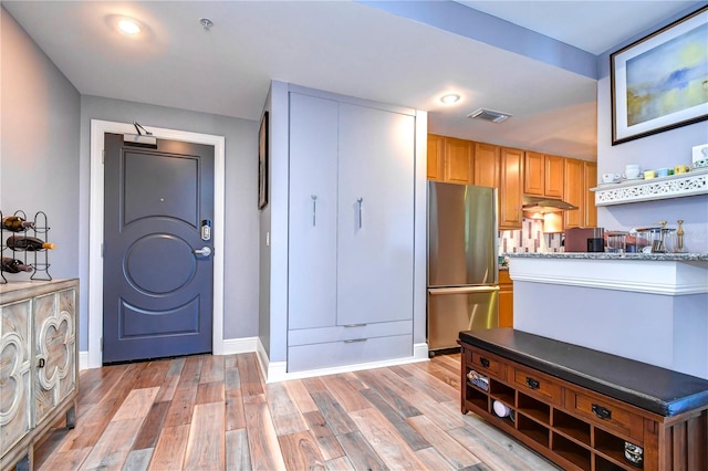 kitchen with light stone countertops, light wood-type flooring, and stainless steel refrigerator