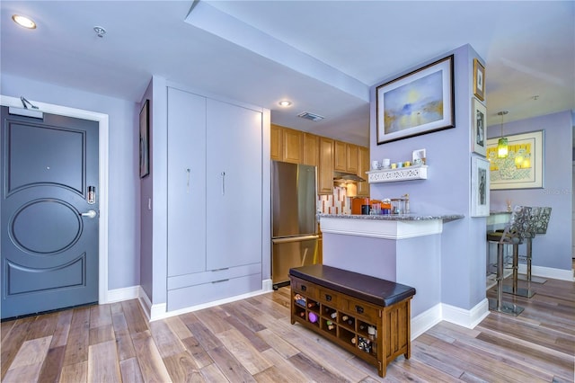 kitchen with light stone countertops, hardwood / wood-style flooring, and stainless steel refrigerator