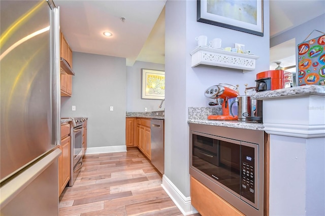 kitchen featuring wall chimney exhaust hood, light stone counters, appliances with stainless steel finishes, and light wood-type flooring