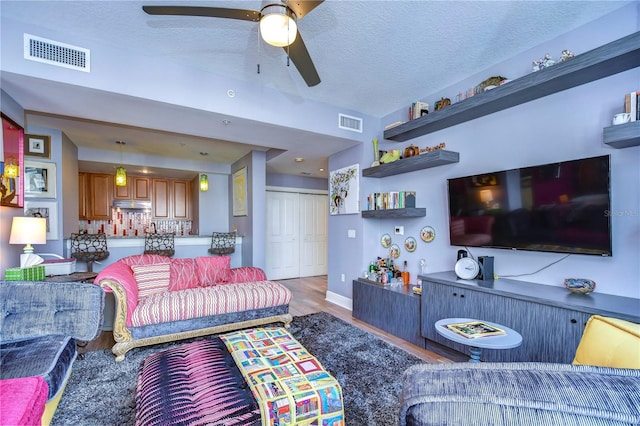 living room with hardwood / wood-style floors, ceiling fan, and a textured ceiling