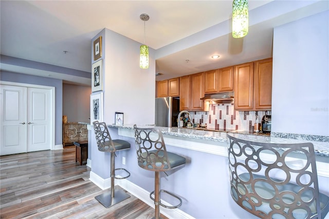 kitchen with backsplash, light stone counters, light hardwood / wood-style floors, and stainless steel refrigerator