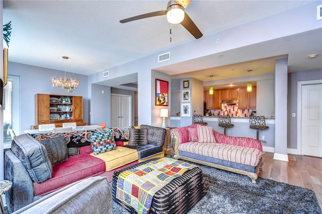 living room with ceiling fan with notable chandelier and hardwood / wood-style floors