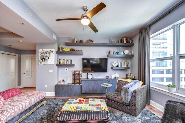 living room with light hardwood / wood-style floors, ceiling fan, and a textured ceiling