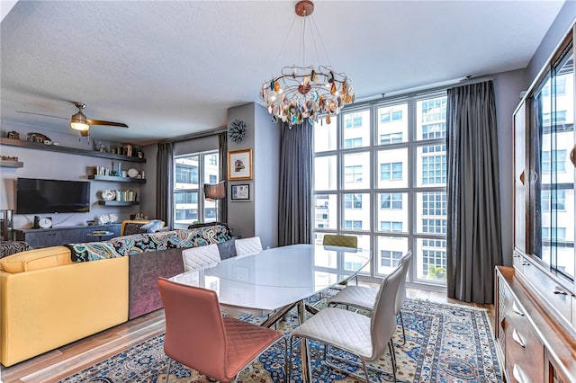 dining space with hardwood / wood-style flooring, ceiling fan with notable chandelier, and a textured ceiling