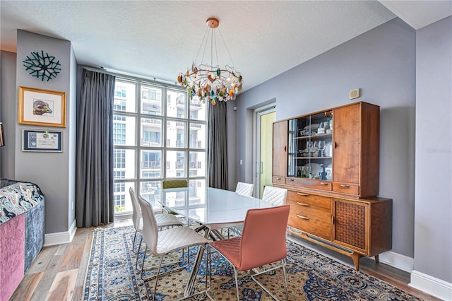 dining area featuring expansive windows, a textured ceiling, a notable chandelier, and hardwood / wood-style flooring