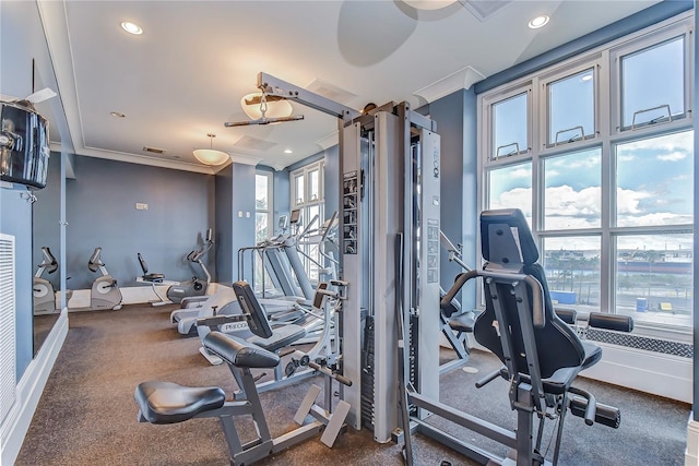 workout area featuring dark carpet, ornamental molding, and a healthy amount of sunlight