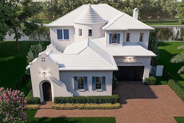 view of front of home with decorative driveway, a water view, a front yard, and stucco siding