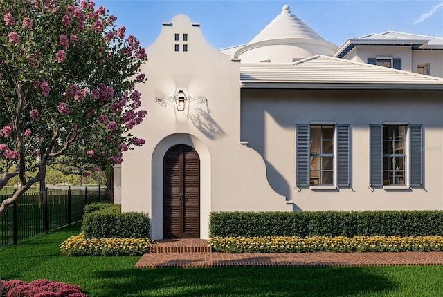 view of exterior entry featuring a yard, fence, and stucco siding