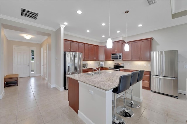 kitchen with a kitchen bar, light stone countertops, a center island with sink, appliances with stainless steel finishes, and hanging light fixtures