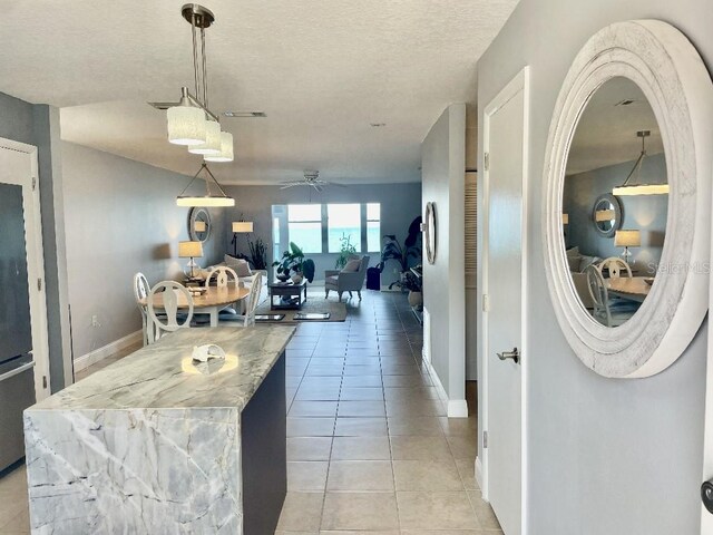 kitchen with hanging light fixtures, ceiling fan, light tile floors, a textured ceiling, and light stone counters