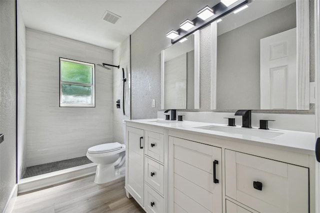 bathroom with double sink vanity, toilet, a tile shower, and wood-type flooring