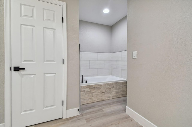 bathroom featuring a relaxing tiled bath and hardwood / wood-style floors