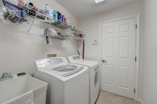 laundry area with light tile patterned flooring, a textured ceiling, sink, and washing machine and clothes dryer