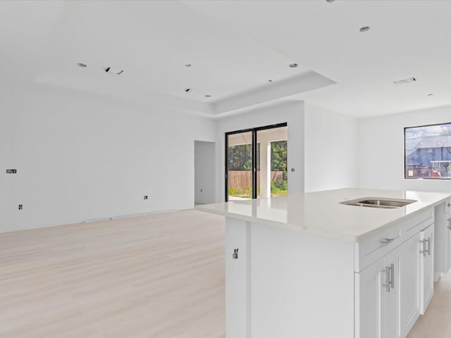 kitchen with white cabinetry, a center island with sink, light hardwood / wood-style floors, and light stone countertops