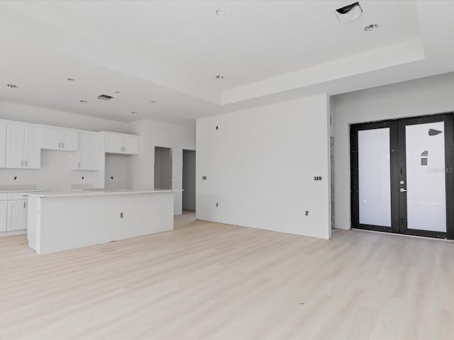 unfurnished living room with a raised ceiling and light wood-type flooring