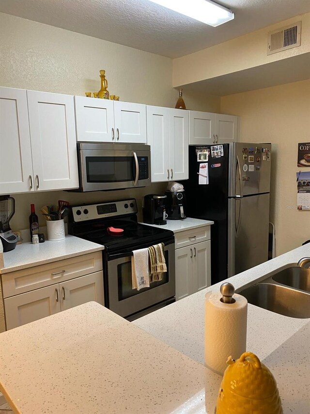 kitchen featuring a textured ceiling, white cabinets, appliances with stainless steel finishes, and sink