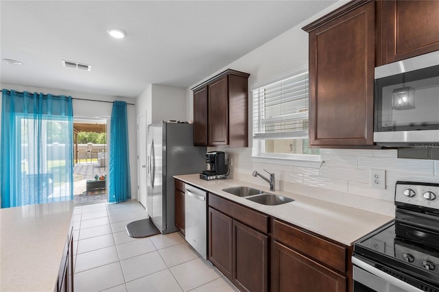 kitchen with dark brown cabinetry, sink, decorative backsplash, light tile patterned floors, and appliances with stainless steel finishes