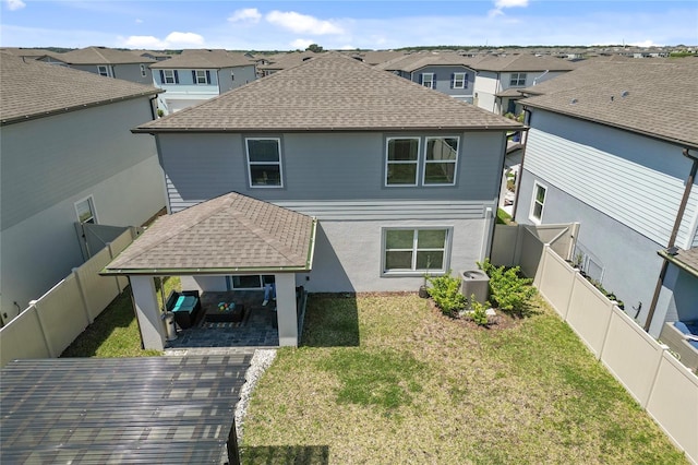 back of house featuring a fenced backyard, a residential view, roof with shingles, and a yard