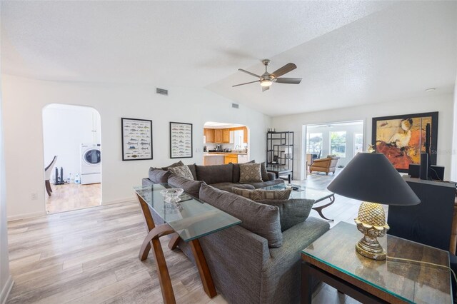 living room with washer / dryer, ceiling fan, light wood-type flooring, and vaulted ceiling