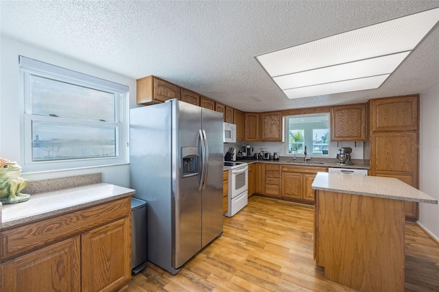 kitchen with white appliances, sink, light wood-type flooring, a kitchen island, and a textured ceiling