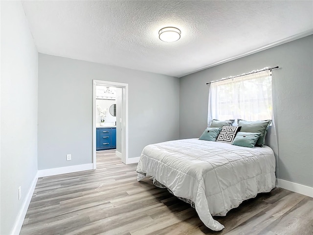 bedroom with light hardwood / wood-style floors, ensuite bath, and a textured ceiling