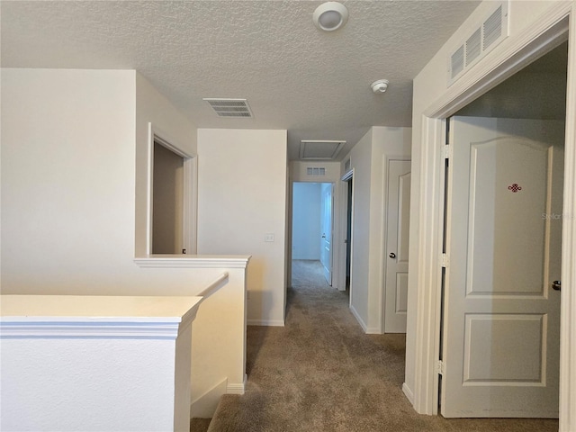 hallway with a textured ceiling and dark colored carpet