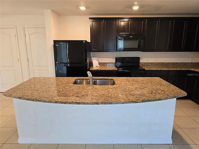 kitchen featuring light tile patterned floors, dark stone counters, a kitchen island with sink, and black appliances