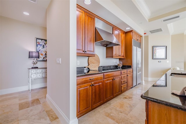 kitchen featuring crown molding, wall chimney exhaust hood, black electric cooktop, and dark stone counters