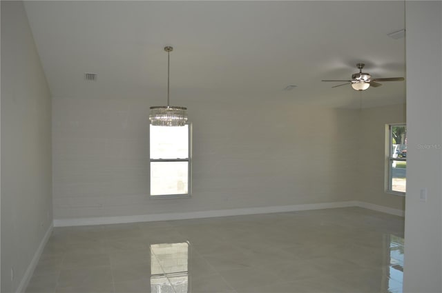 tiled spare room featuring plenty of natural light and ceiling fan with notable chandelier