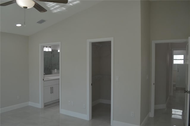 unfurnished bedroom with ceiling fan, connected bathroom, light tile floors, a spacious closet, and vaulted ceiling