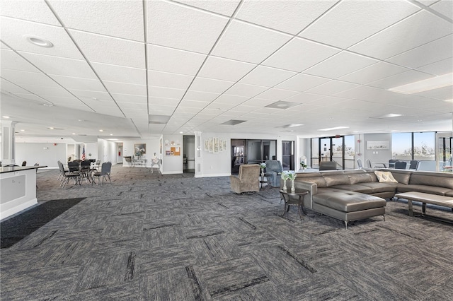 living area featuring dark carpet, a paneled ceiling, and baseboards