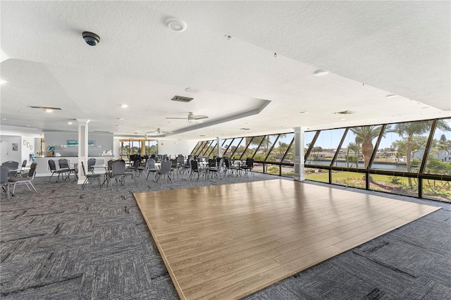 exercise room featuring a water view, a wall of windows, carpet flooring, and a textured ceiling