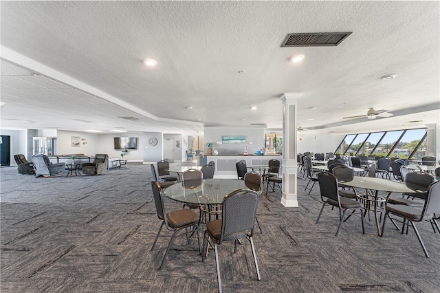 carpeted dining space with ceiling fan, a textured ceiling, and ornate columns