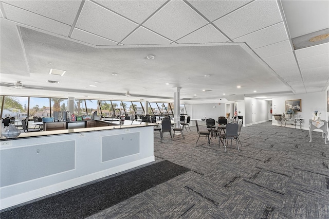 interior space featuring decorative columns, carpet floors, a drop ceiling, and ceiling fan