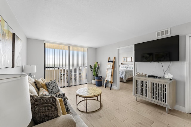 living area featuring wood finish floors, visible vents, expansive windows, a textured ceiling, and baseboards