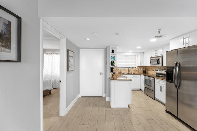 kitchen with appliances with stainless steel finishes, dark countertops, white cabinets, and light wood finished floors