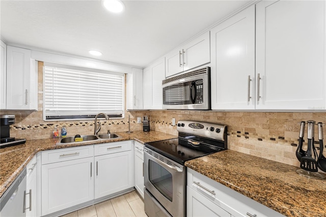 kitchen featuring a sink, white cabinets, appliances with stainless steel finishes, decorative backsplash, and dark stone countertops