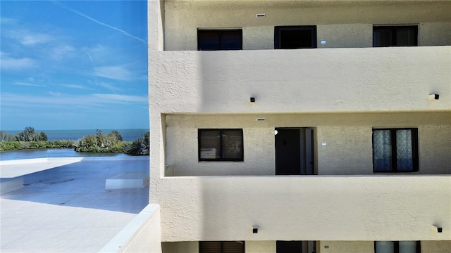 rear view of property with a water view, a balcony, and stucco siding