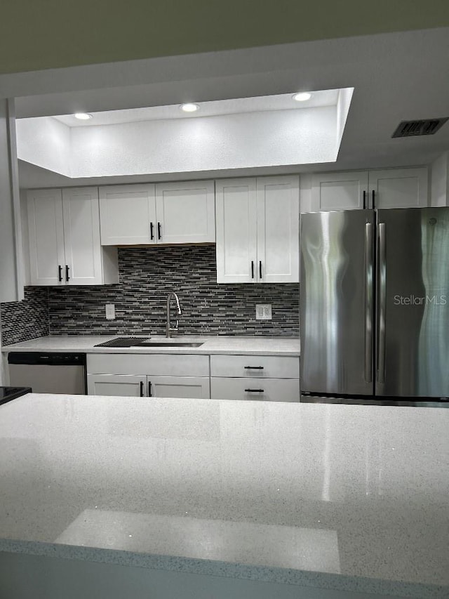 kitchen with stainless steel appliances, white cabinetry, backsplash, a raised ceiling, and sink